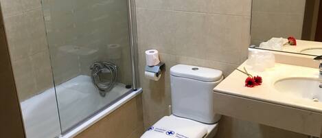 Een badkamer met toilet, een douche met glazen wand, wastafel en spiegel.