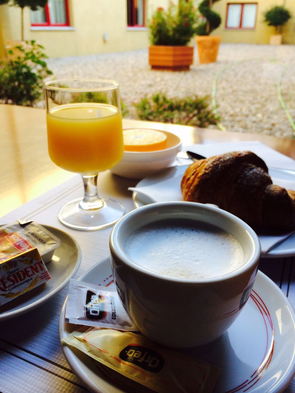 A breakfast setting with a cup of coffee, a glass of orange juice, a croissant, and a plate with a bowl of soup.