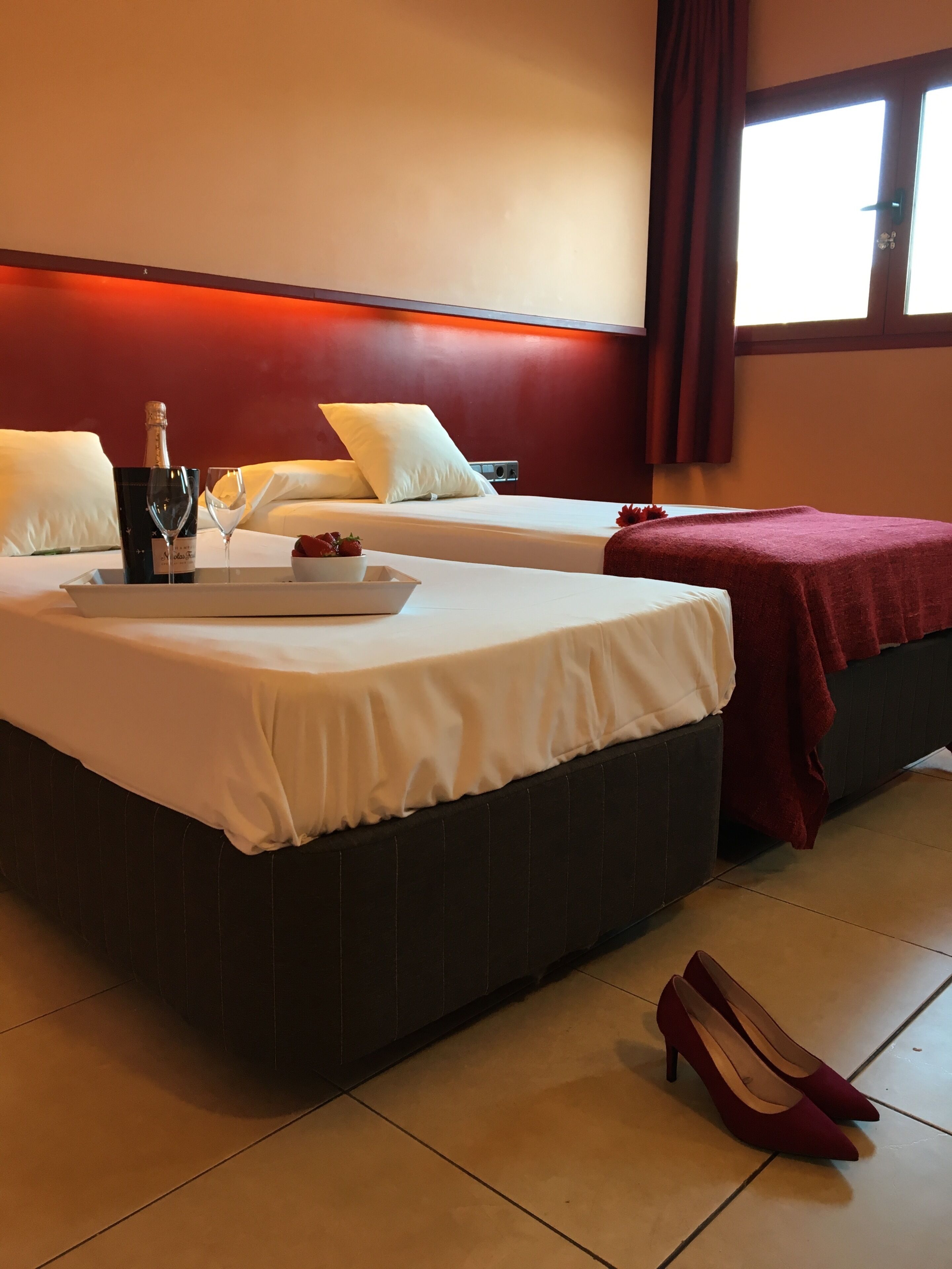 Habitación de hotel con dos camas, un atril con una botella y vasos, y un par de zapatos en el suelo.