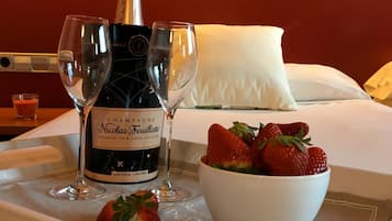 A tray with a bottle of champagne, two glasses, and a bowl of strawberries on a hotel bed.