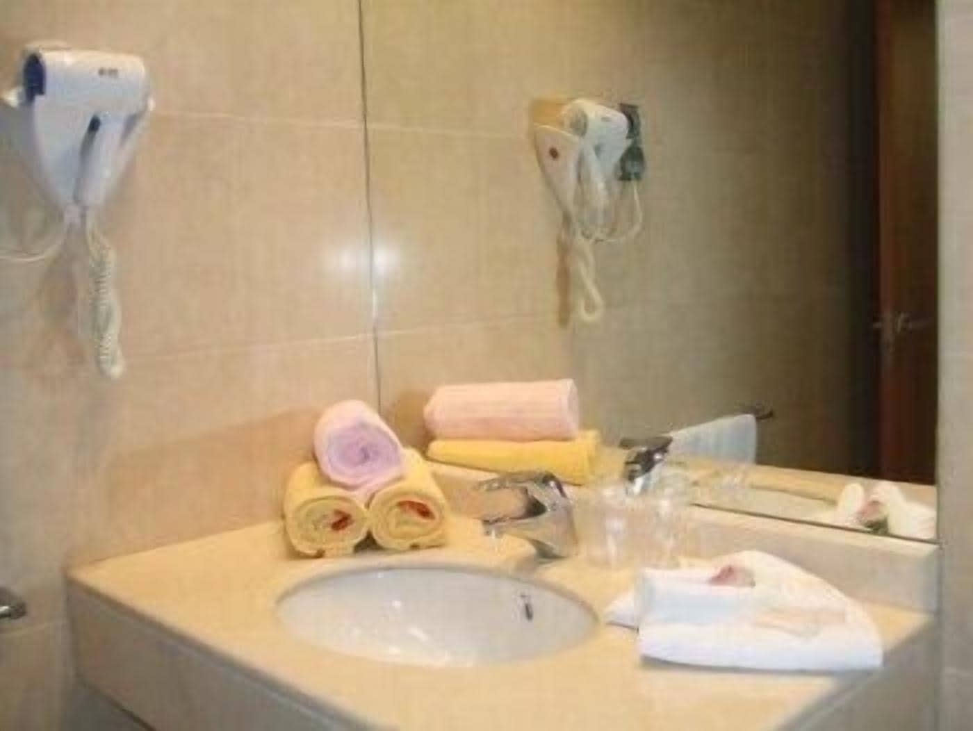 Un baño con un lavabo, dos secadores de pelo sujetos a la pared y varias toallas apiladas sobre la encimera.
