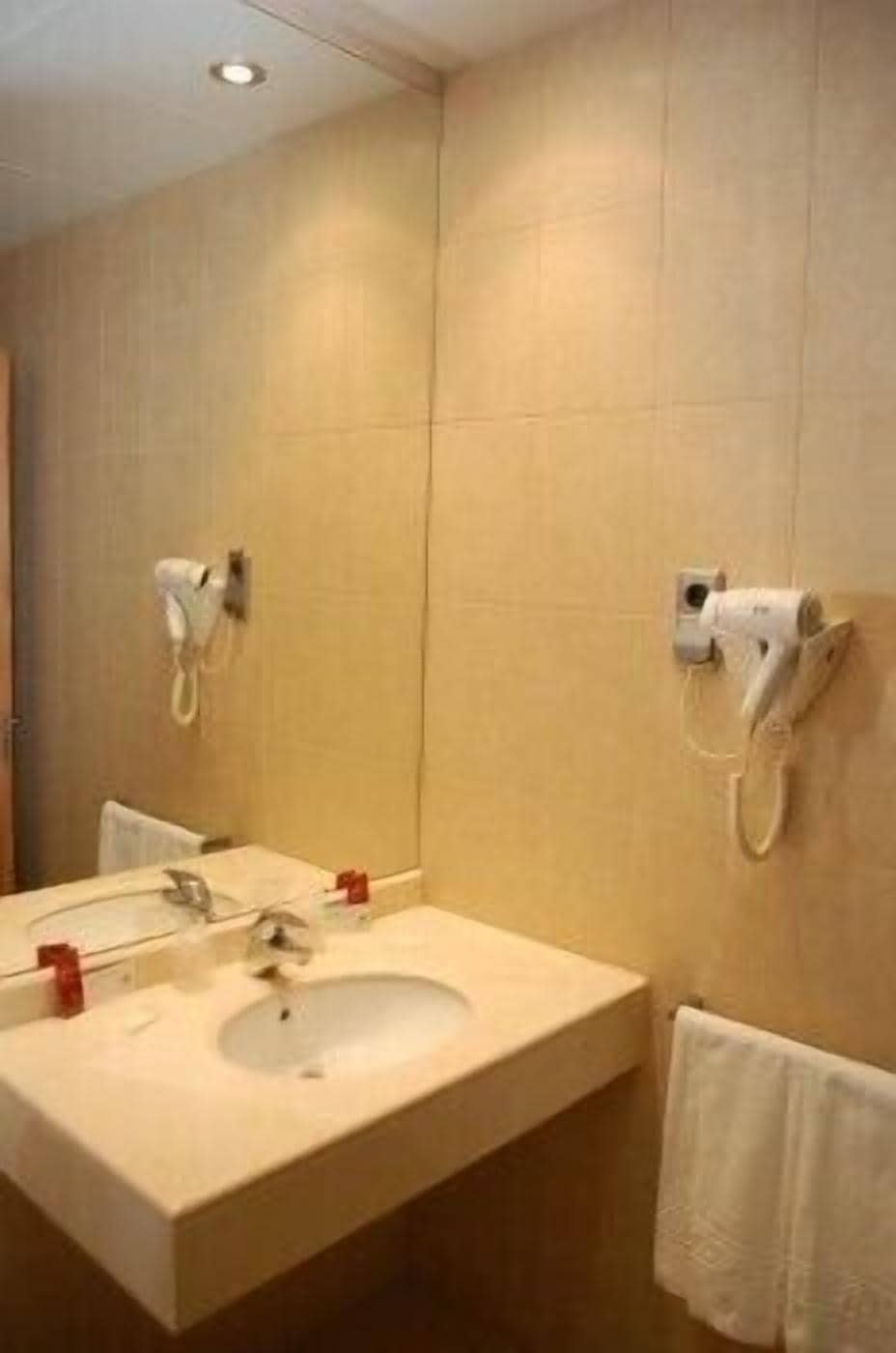 A bathroom with a sink, mirror, towel rack, and two hair dryers mounted on the wall.