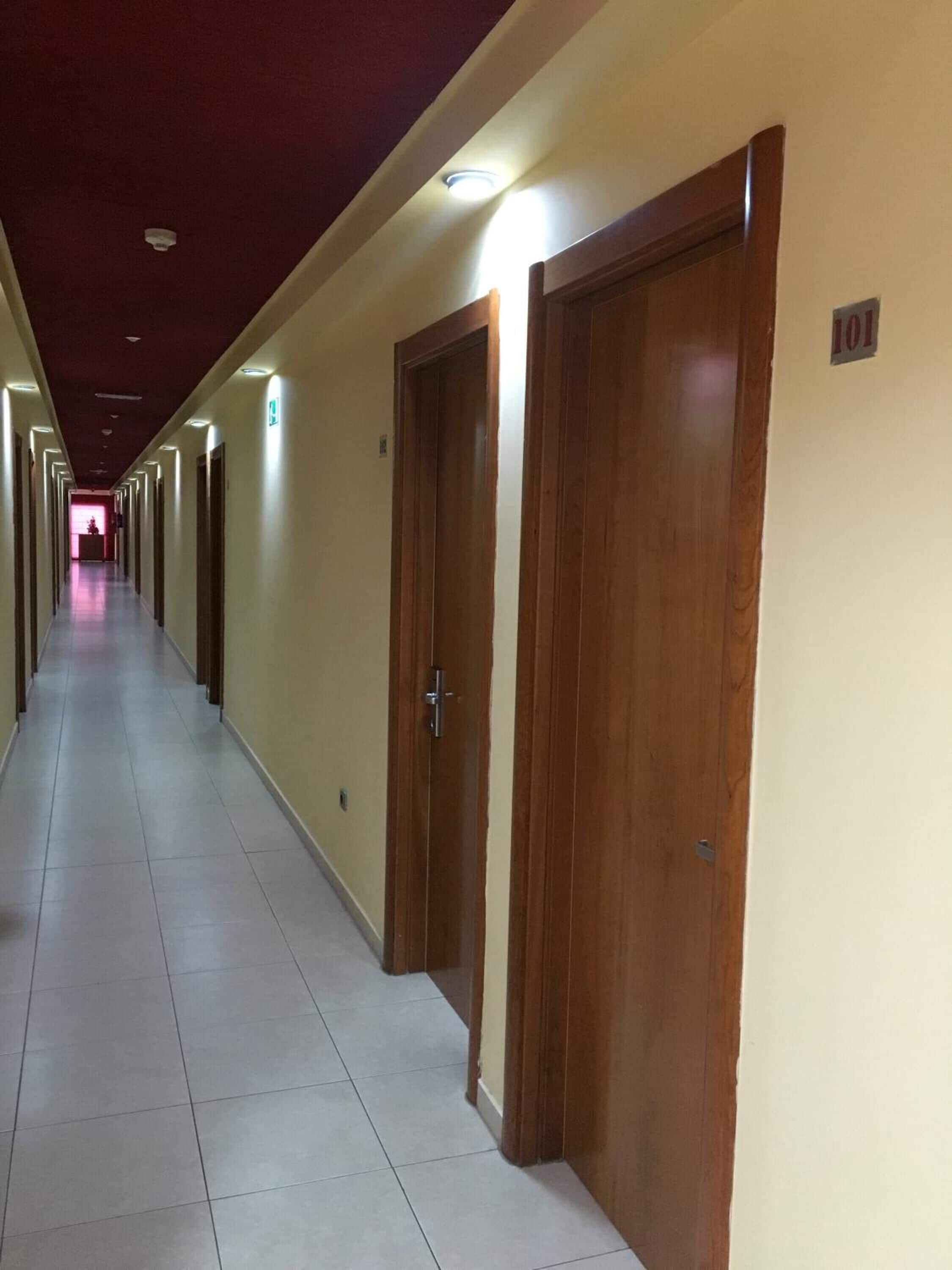 A long, narrow hotel corridor with wooden doors, numbered 101, and a tiled floor.