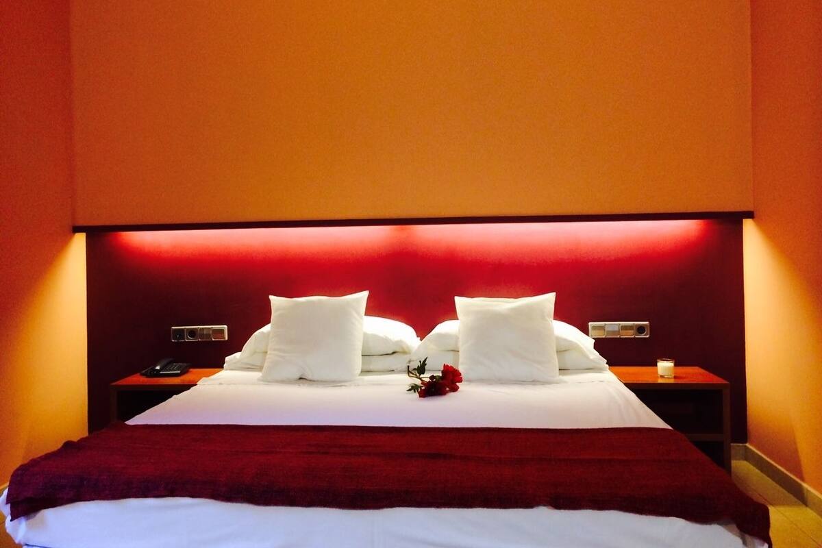 A hotel room with a large bed, two bedside tables, and a red wall.