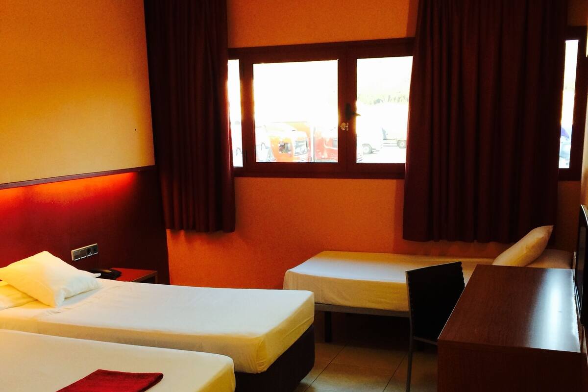 A hotel room with two beds, a desk, and a window with curtains.