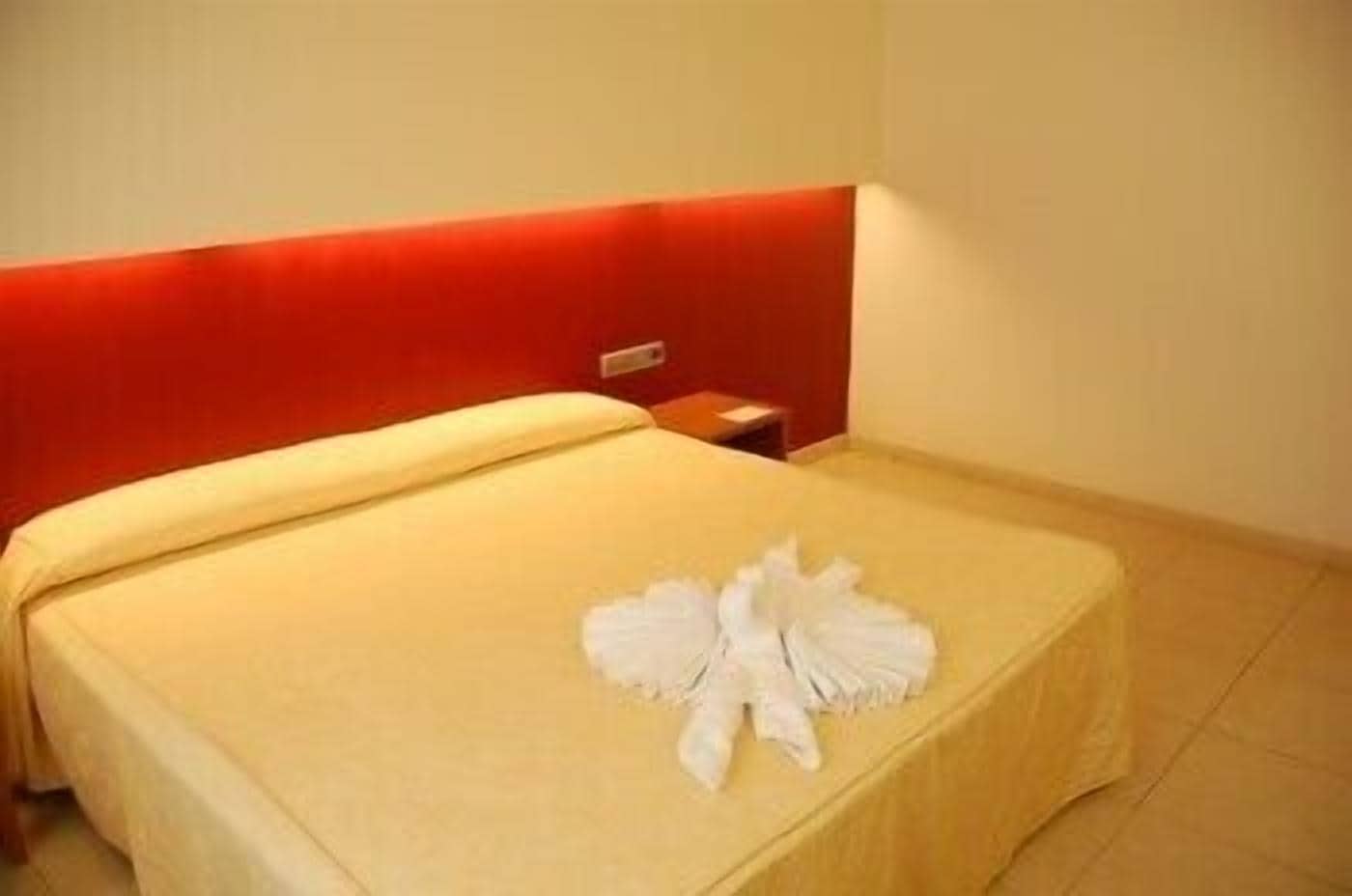 Une chambre d’hôtel avec un lit, une tête de lit rouge et une serviette blanche posée sur le lit.