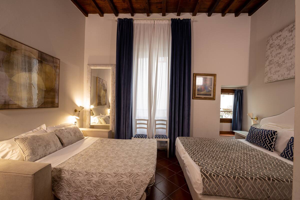 Een hotelkamer met twee bedden, een groot abstract schilderij, een spiegel en een raam met gordijnen.