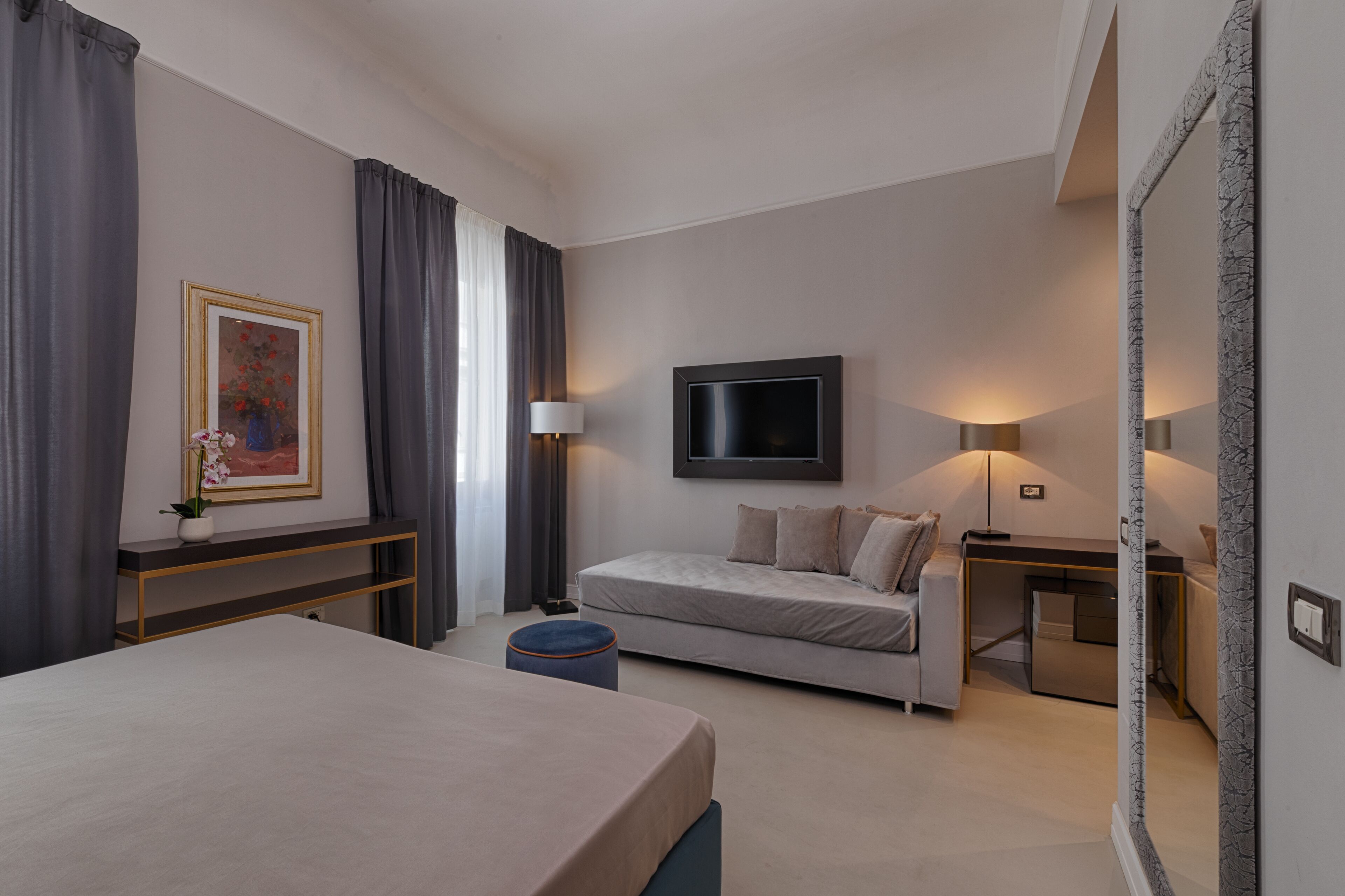A modern hotel room with a bed, a sofa, a TV, and a desk with a lamp.