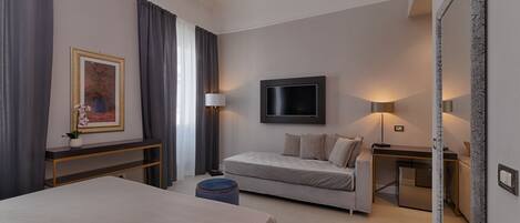 A modern hotel room with a bed, a sofa, a TV, and a desk with a lamp.