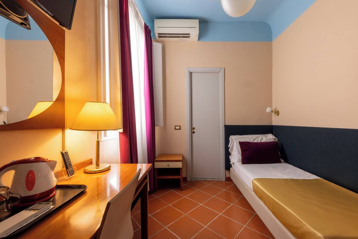 Een hotelkamer met een bed, een bureau met een lamp, een telefoon en een airconditioning.