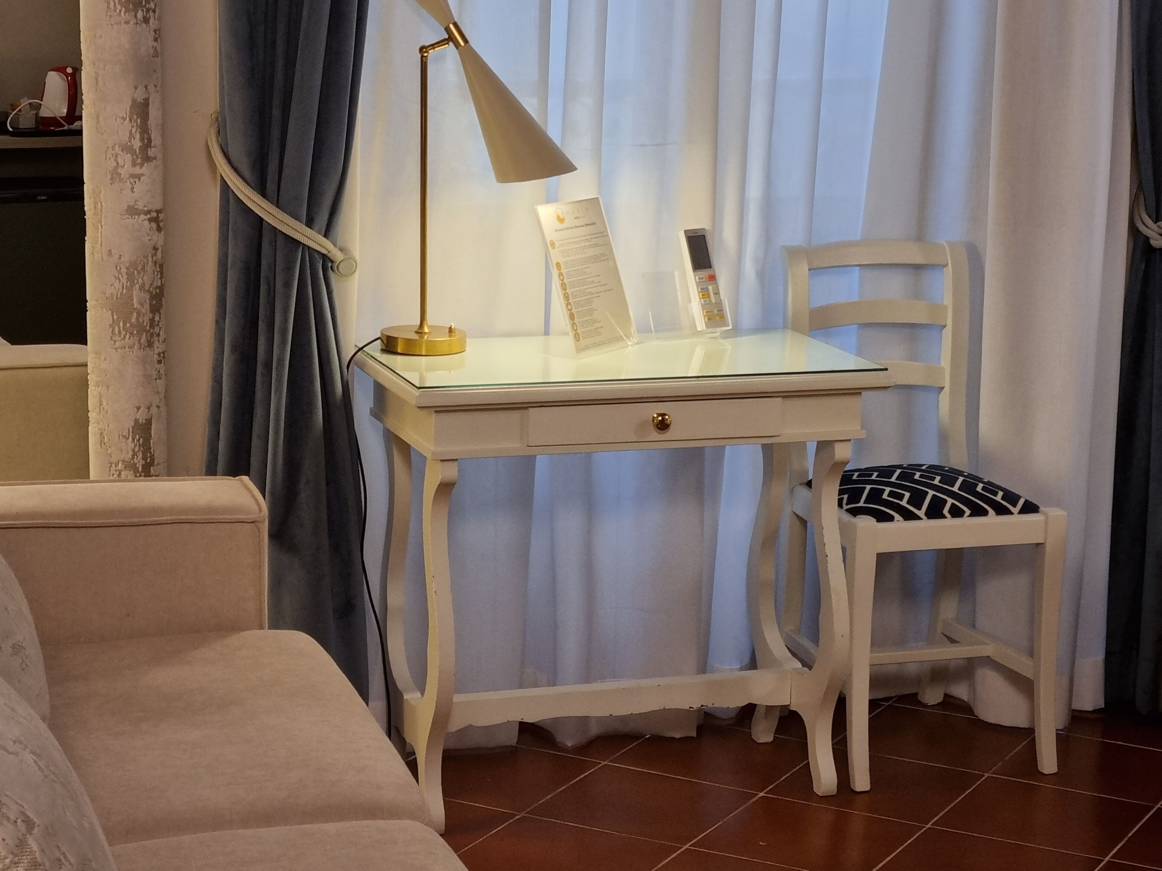 A room with a white desk, a chair, a lamp, and a window with curtains.