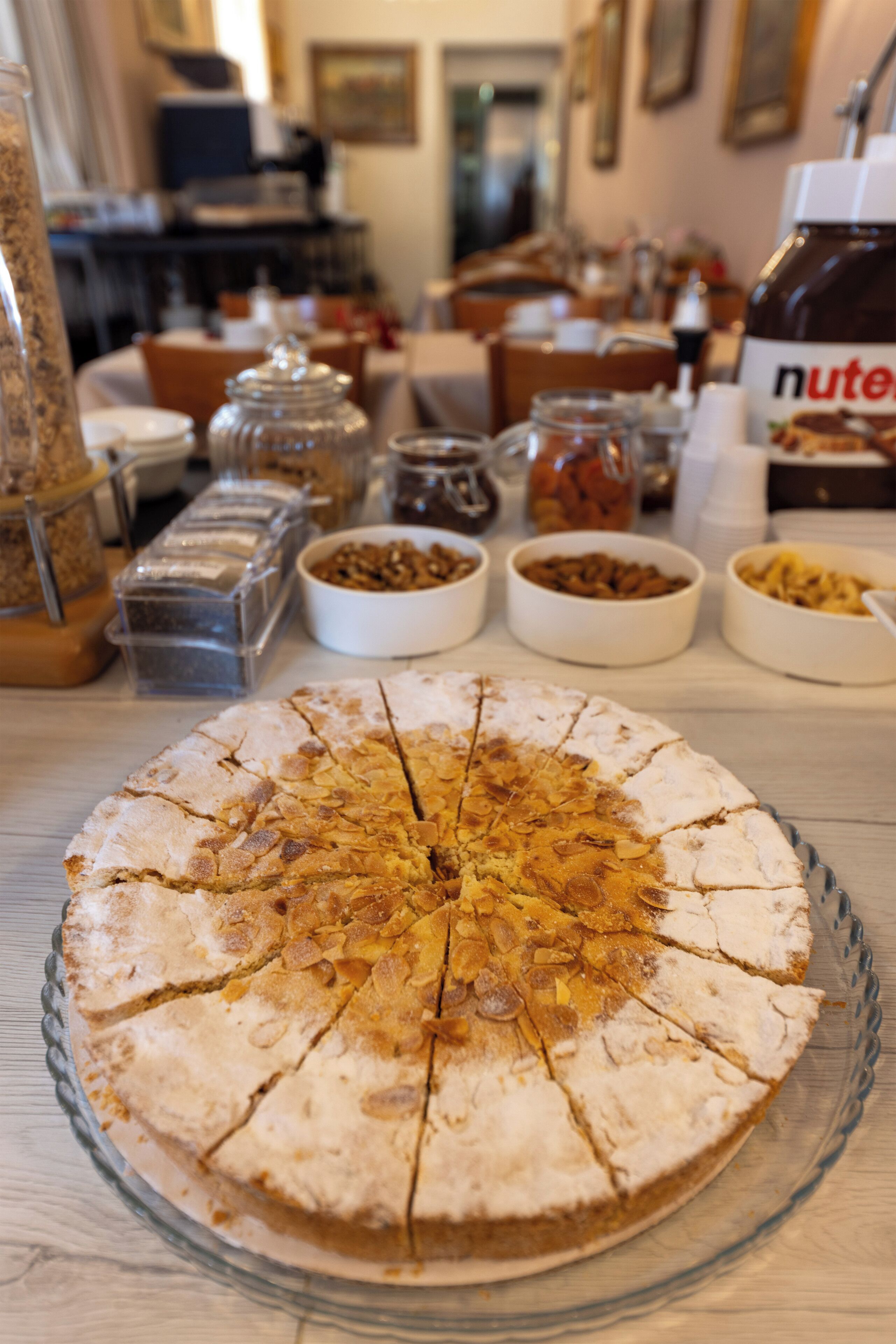 Un pastel redondo con porciones cortadas sobre un plato de vidrio, rodeado de varios recipientes y frascos de comida.