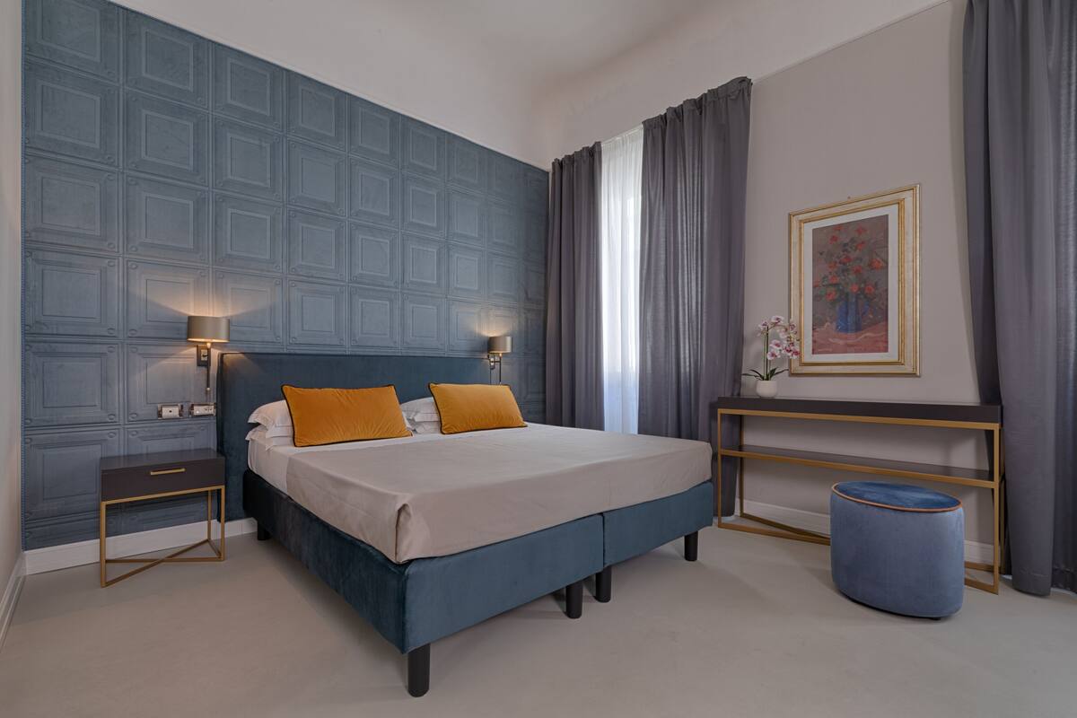 Een slaapkamer met een groot bed, twee bedlampen, een nachtkastje, een kleine tafel met een vaas en een schilderij aan de muur.