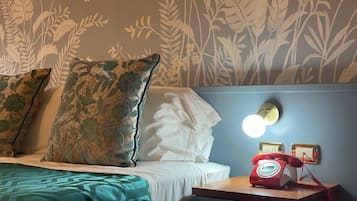 Ein Hotelzimmer mit Bett, Kissen, einem Nachttisch mit einem roten Wählscheibentelefon und einer Wand mit floralem Wandpapier.