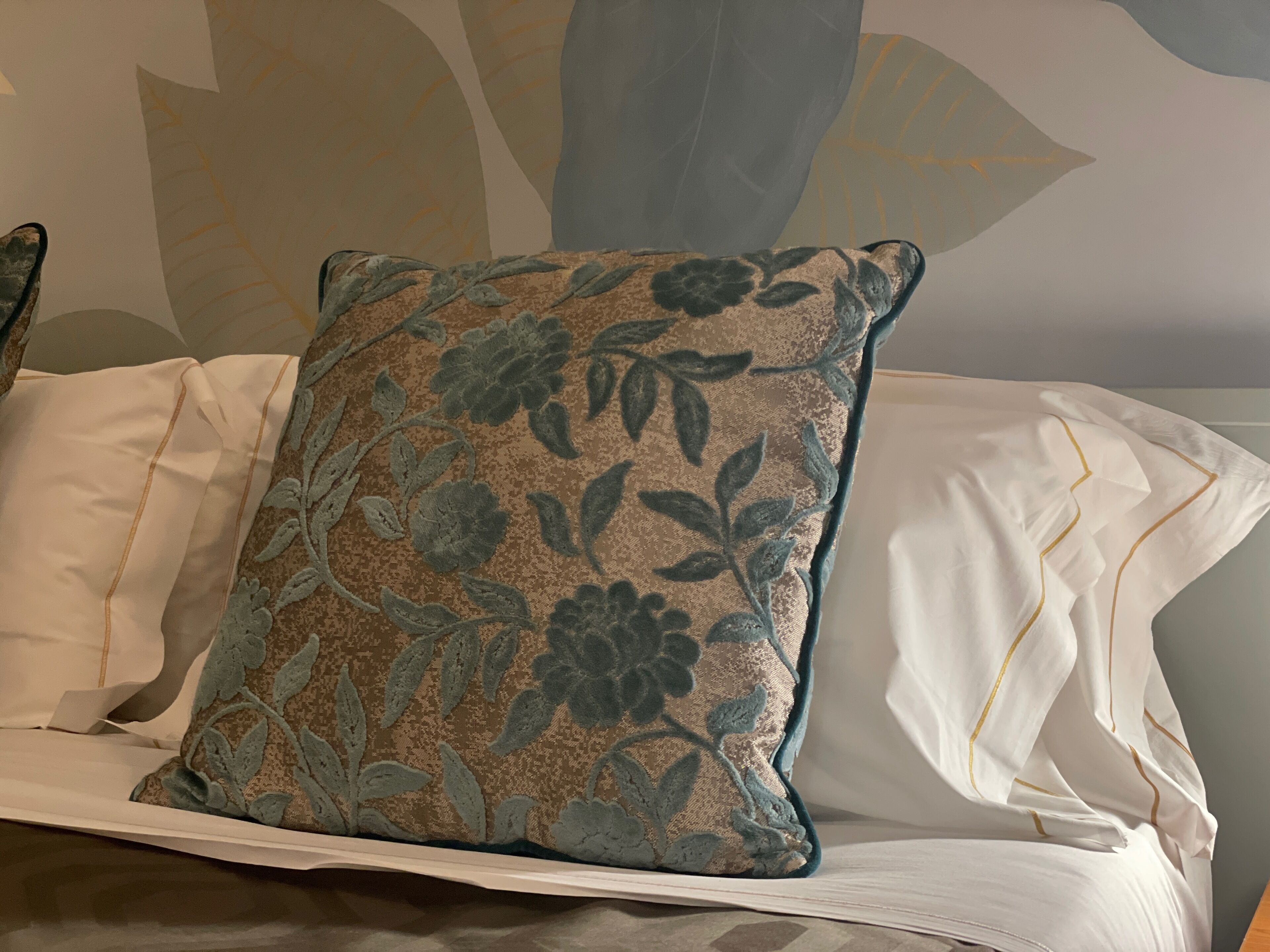 Un lit avec un coussin à motifs floraux et du linge de lit blanc.