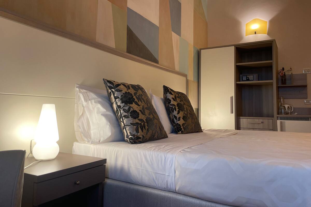 Een hotelkamer met een bed, nachtkastje, lamp en een kledingkast.