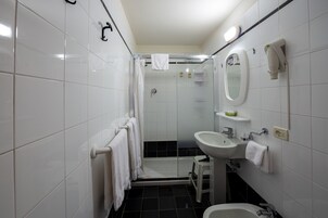 Un bagno moderno con piastrelle bianche, cabina doccia in vetro, lavabo e specchio.