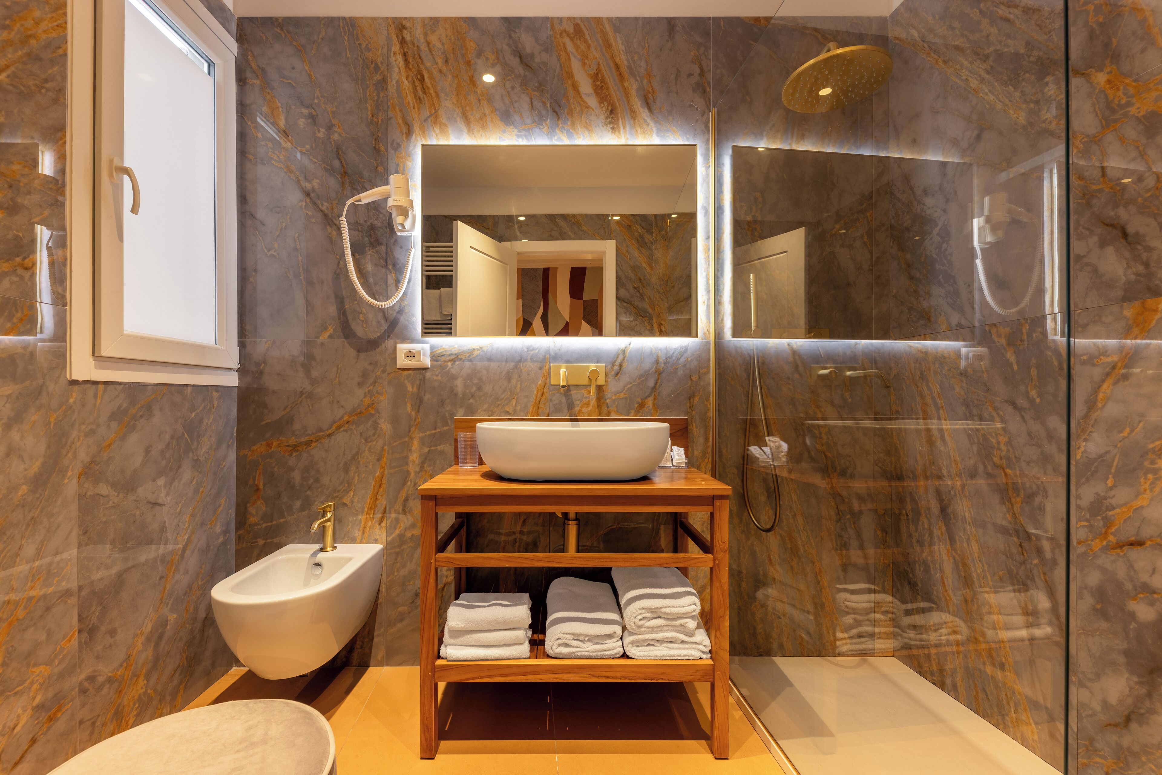 Une salle de bain moderne avec un pare-baignoire en marbre, un meuble-lavabo en bois, un bidet et une douche à l’italienne.