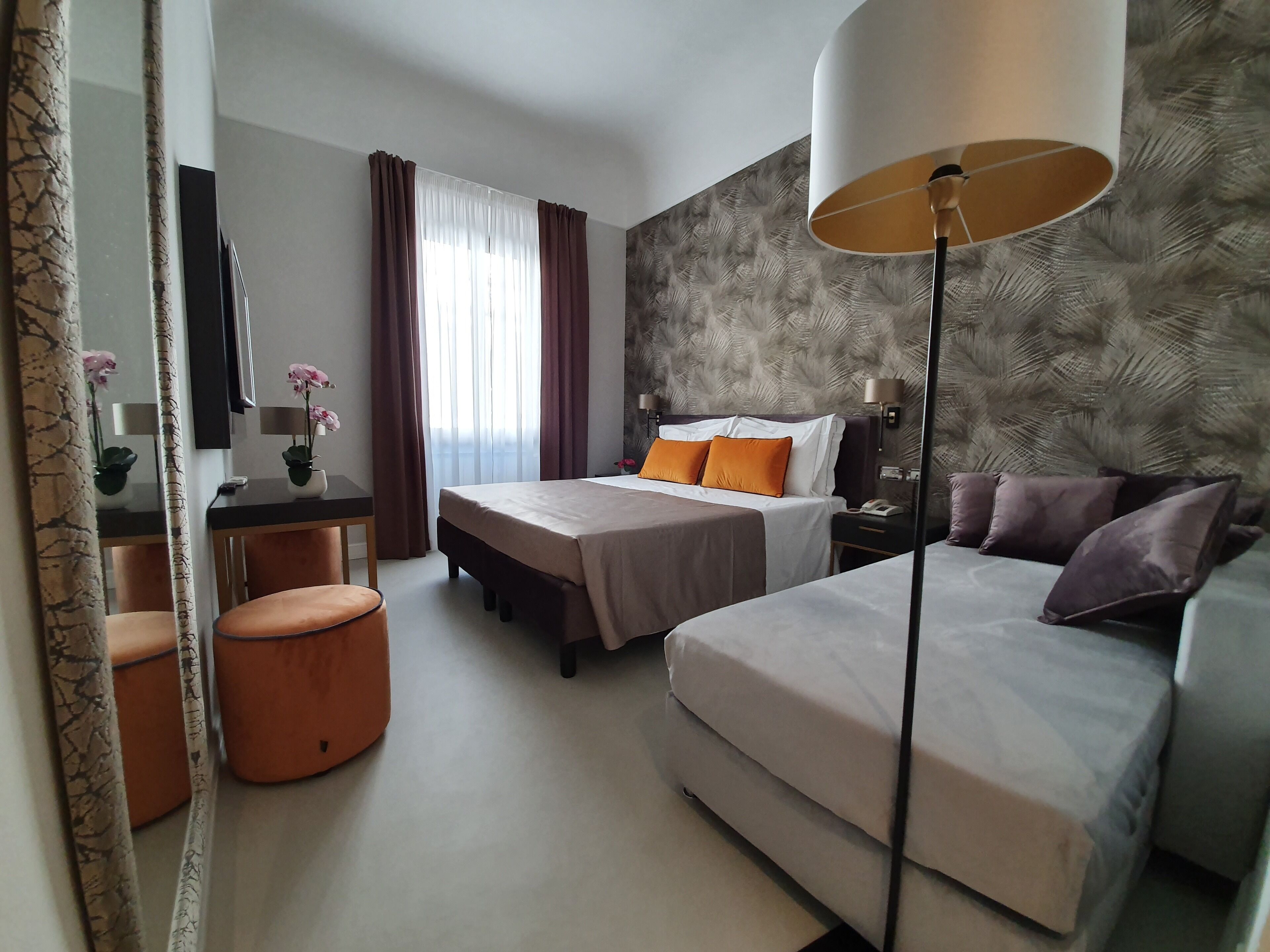 A hotel room with two beds, a desk, a chair, a lamp, and a mirror.