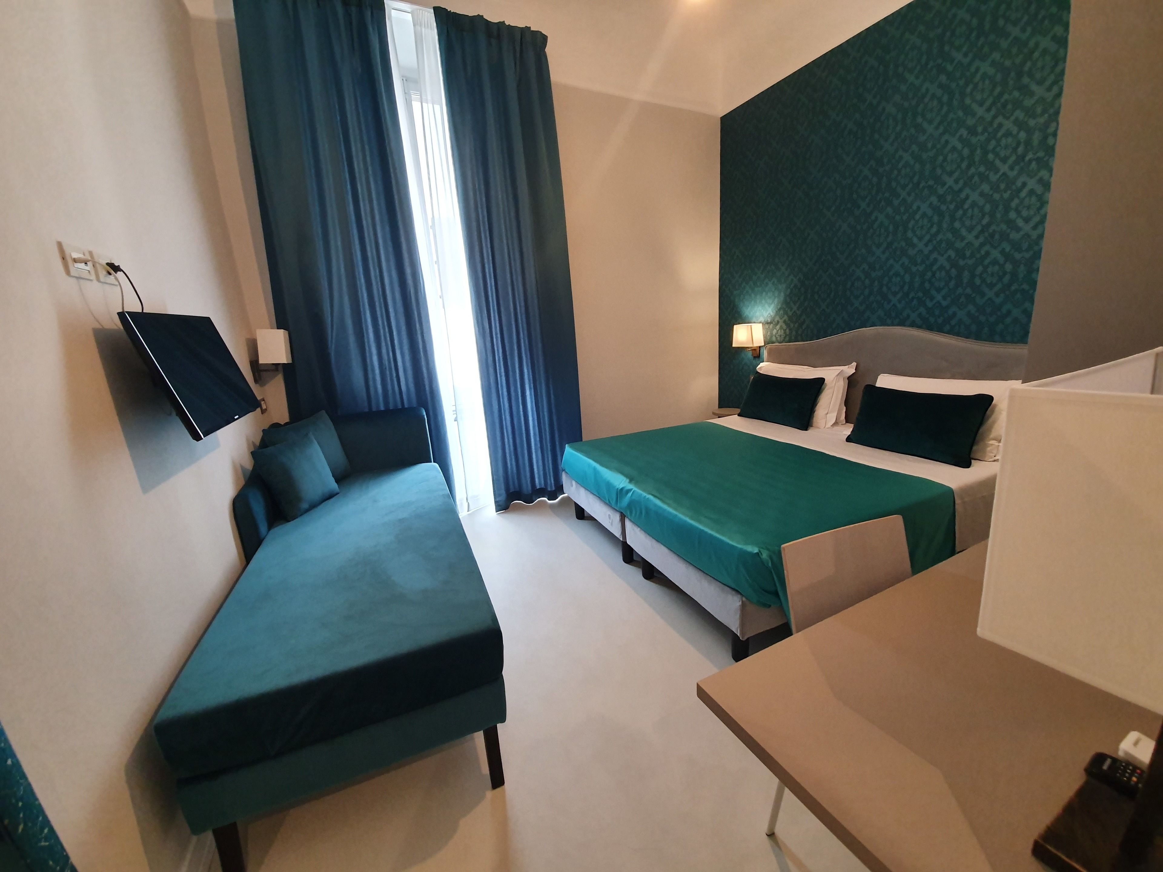A hotel room with a bed, a desk, a TV, and a window with curtains.