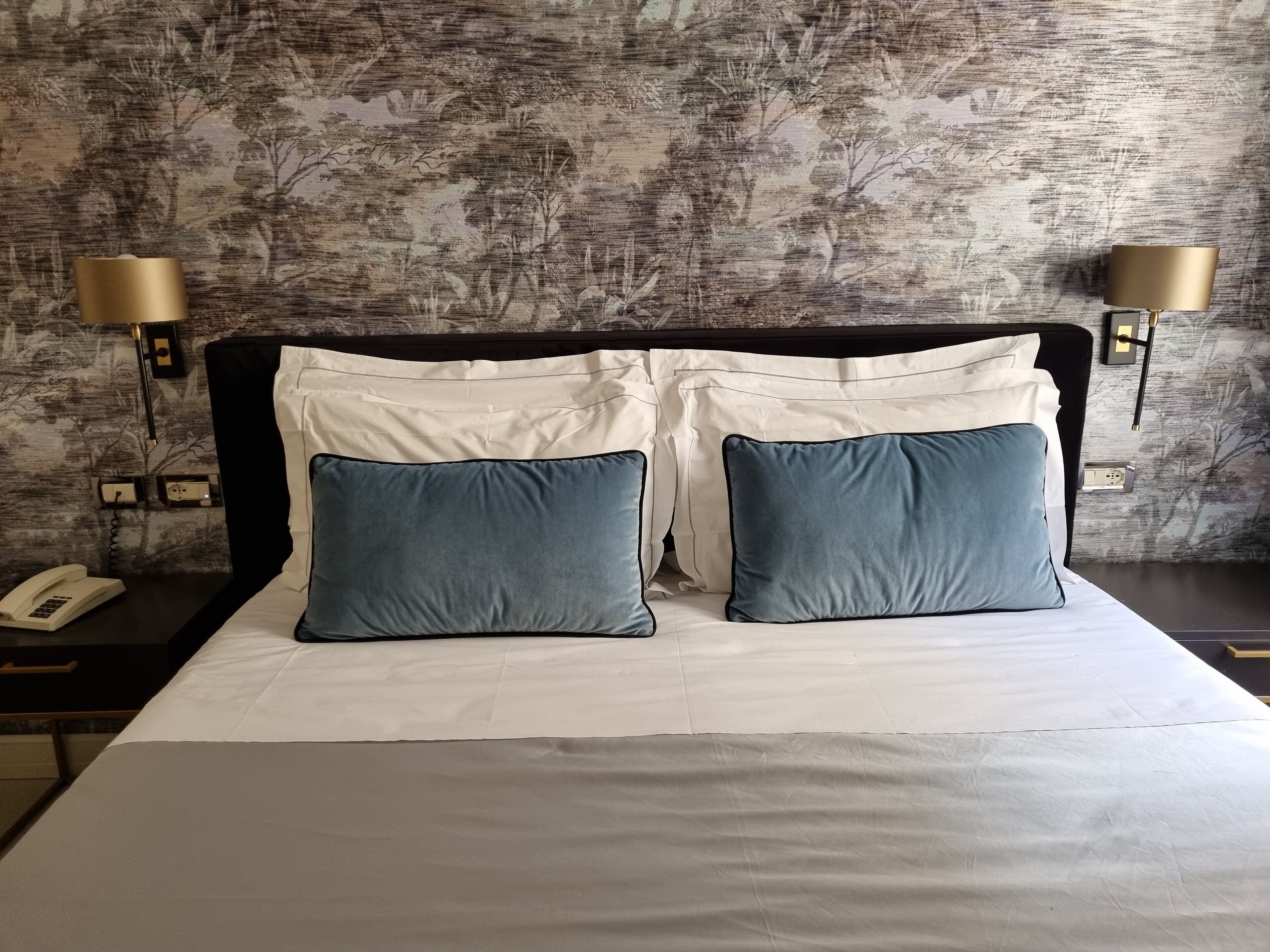 A neatly made bed with two pillows, a bedside lamp, and a phone on a nightstand.