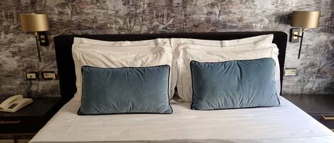 A neatly made bed with two pillows, a bedside lamp, and a phone on a nightstand.
