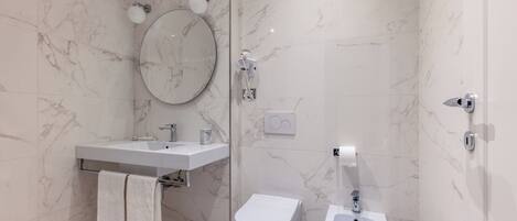 A modern bathroom with a toilet, bidet, and a round mirror.