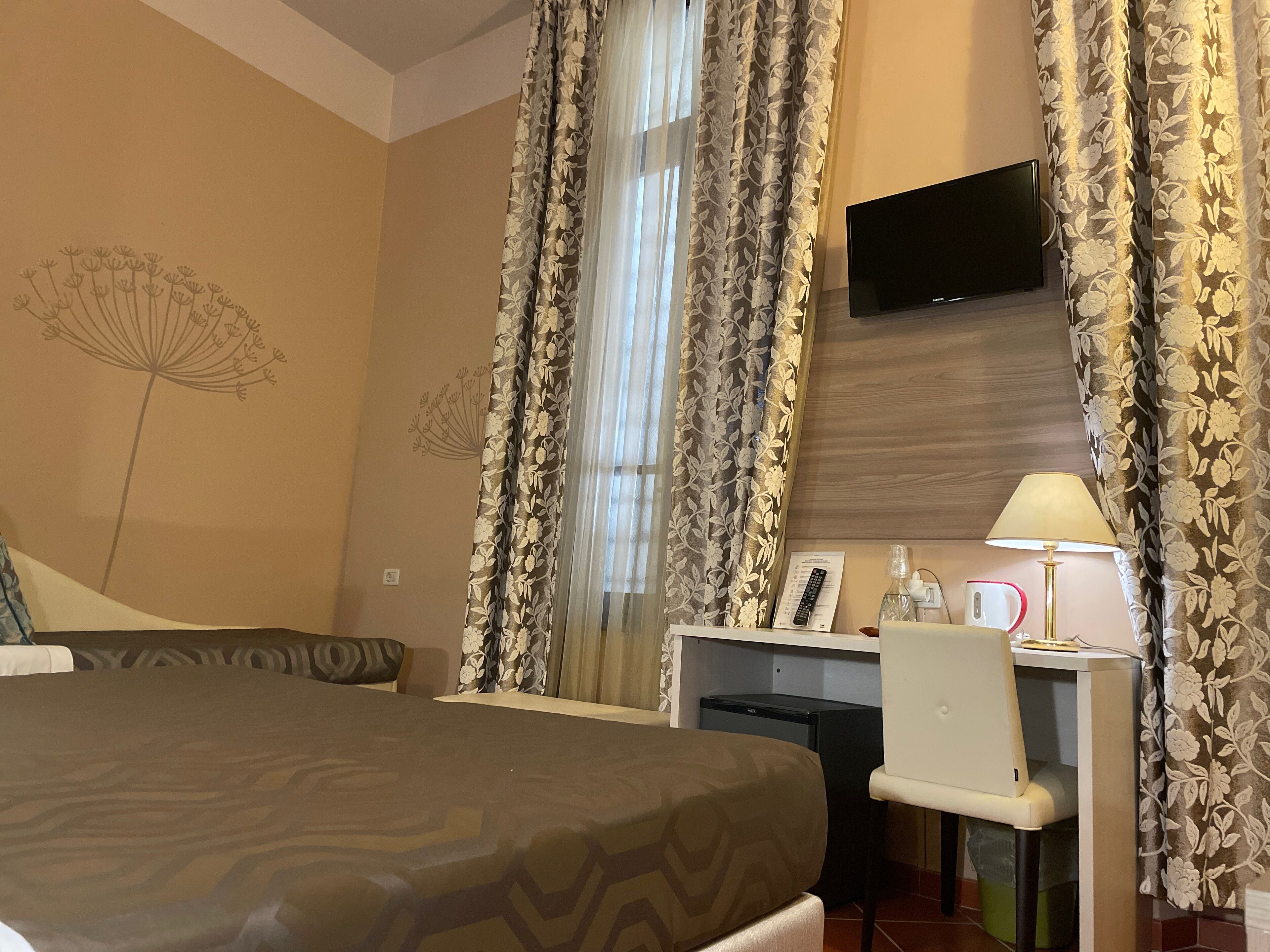 A hotel room with a bed, desk, chair, TV, and curtains.