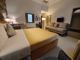 Una camera d'albergo con un letto, un divano, una scrivania con una lampada, una televisione e un armadio.