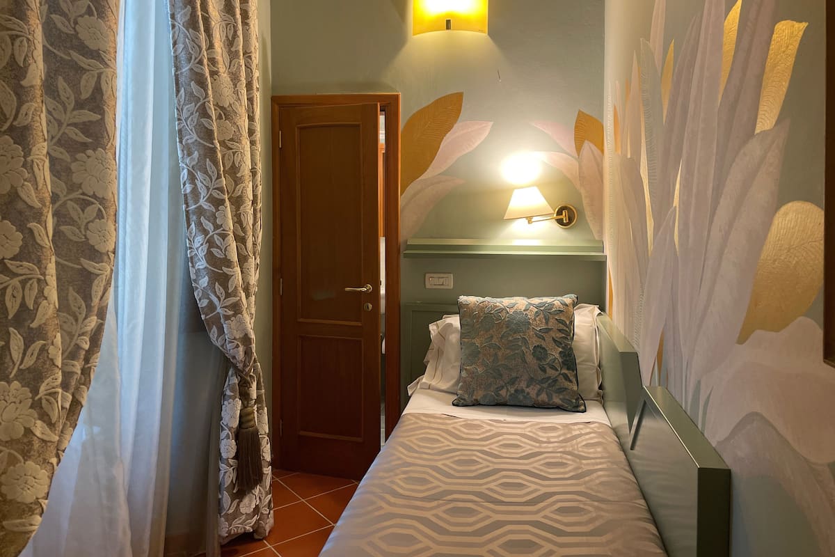 Een slaapkamer met een bed, nachtkastje, een wandlamp en een deur.