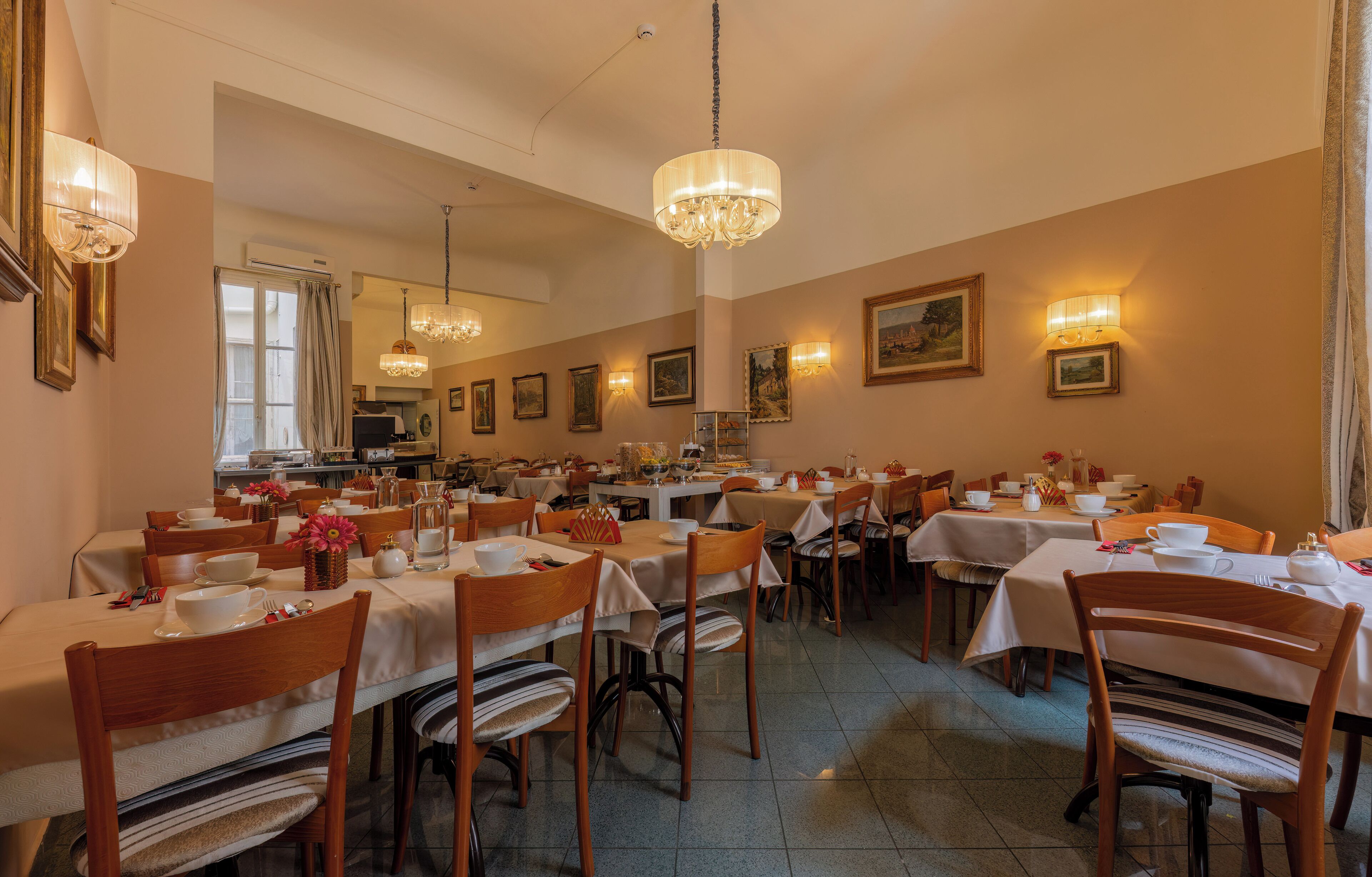 A dining area with multiple tables and chairs, chandeliers, and wall-mounted lights.