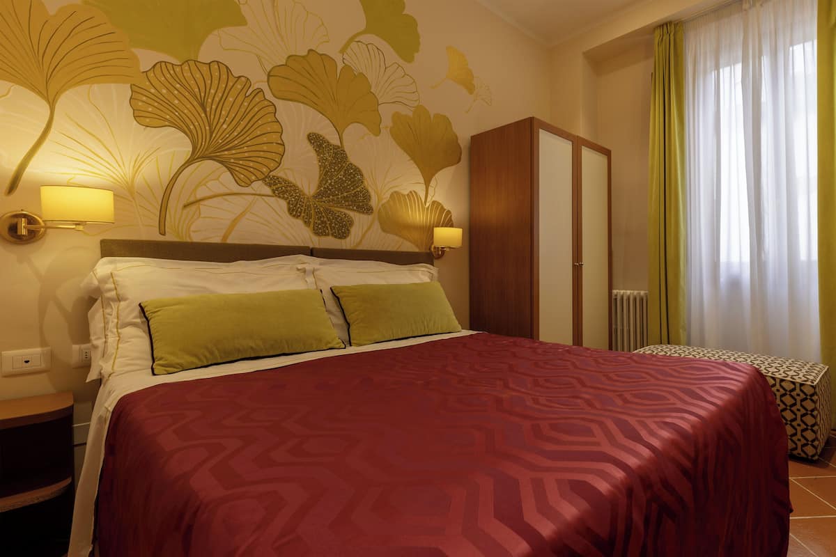 Een hotelkamer met een groot bed, twee wandlampen, een kledingkast en een raam met gordijnen.