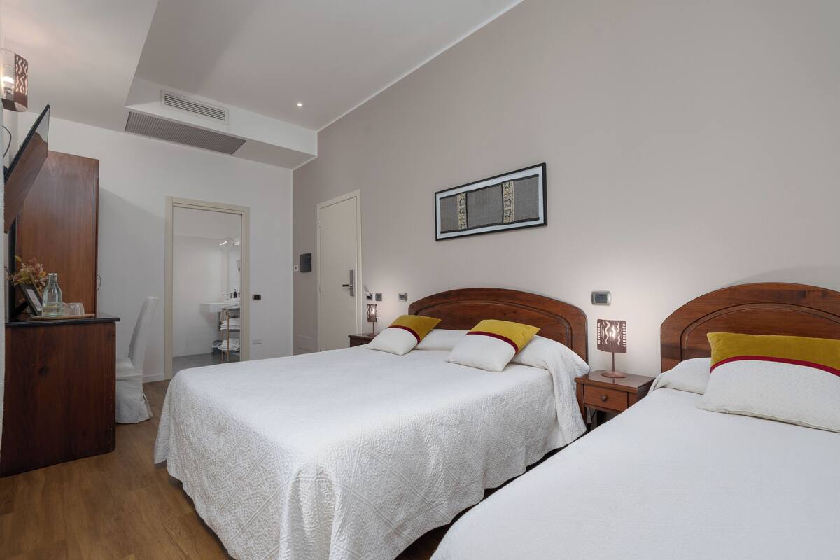 A hotel room with two beds, a wooden dresser, a mirror, a wall-mounted artwork, and a bedside table with a lamp.