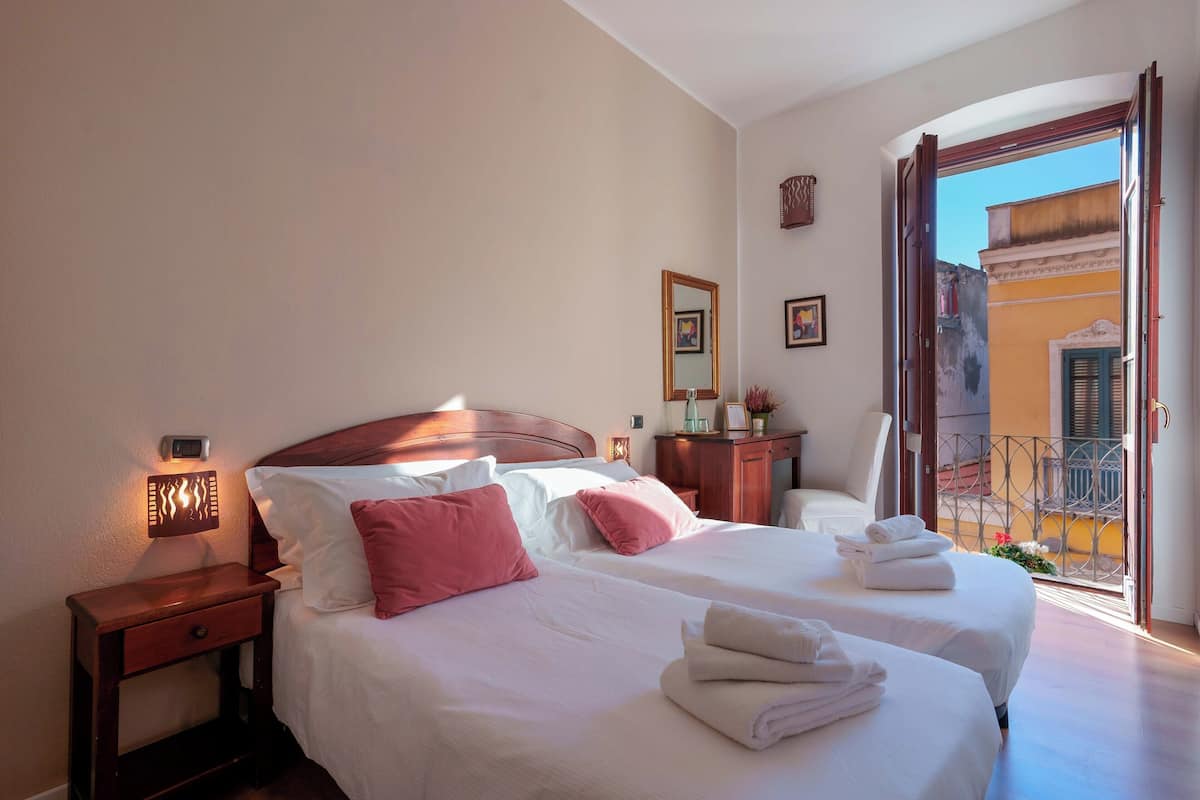 A hotel room with two beds, a nightstand, a bedside table, a mirror, and a view of the outside balcony.