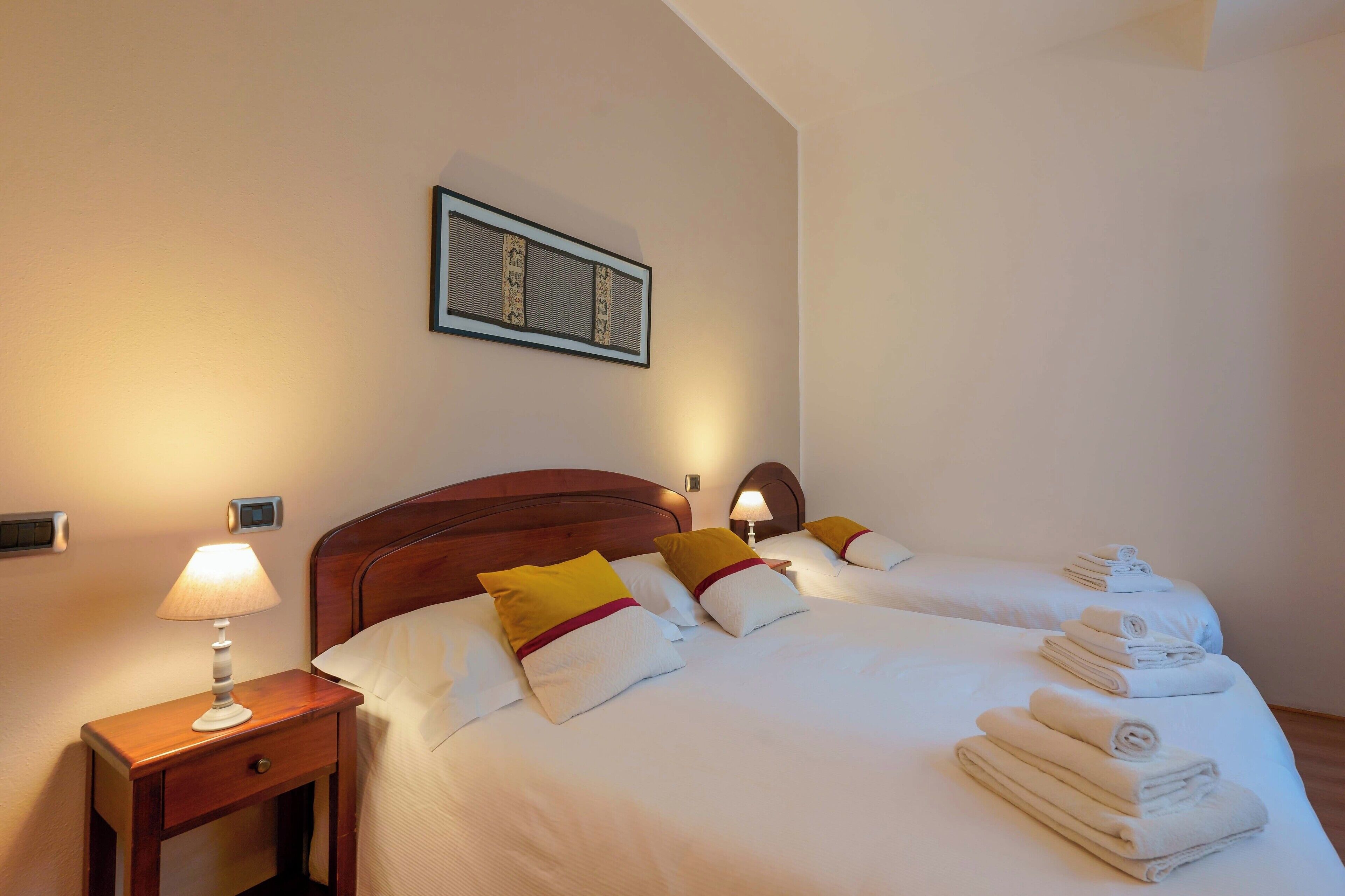 Habitación de hotel con dos camas, una mesita de noche con lámpara y un cuadro enmarcado en la pared.