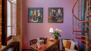 A room with a desk, chair, lamp, and two paintings on the wall.