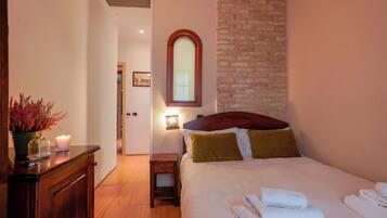 A bedroom with a bed, a nightstand, a mirror, a wall-mounted light, and a brick wall.