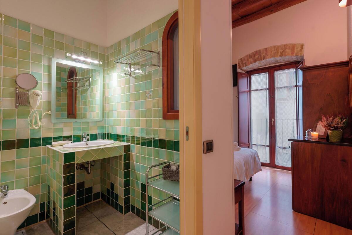A bathroom with green-tiled walls, a white sink, a mirror, and a shower area.