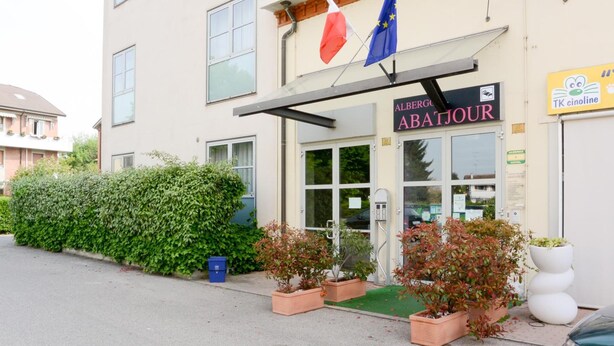 A hotel named "ABATJOUR" with a signboard, flags, and potted plants in front. - Albergo Meublè Abatjour (Mantua)