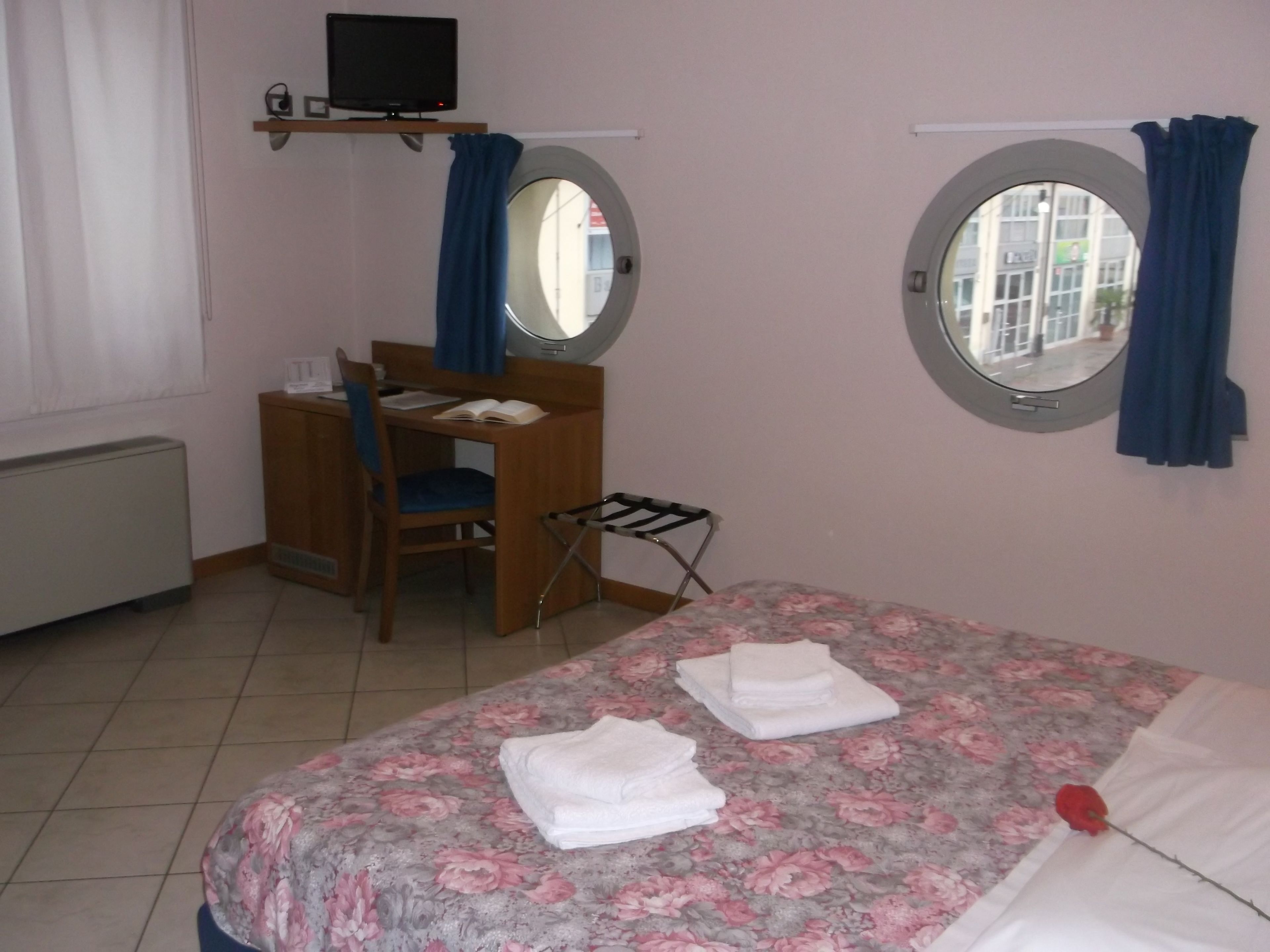 A bedroom with a bed, a desk, a chair, a window, and a television.