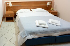 A neatly made bed with white and blue bedding, two bedside tables with lamps, and a small vase with flowers on the nightstand.