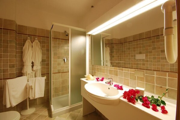 Un baño con cabina de ducha de vidrio, un lavabo con espejo y toallas colgadas en un perchero.