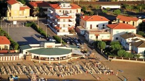 A coastal hotel with multiple buildings, a beach area with umbrellas, and a parking lot. - Del Sole (San Vincenzo)