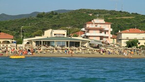 A coastal hotel with multiple floors, beachside location, and a view of the sea and hills in the background. - Del Sole (San Vincenzo)