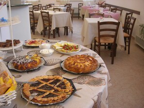 Comedor con varias mesas dispuestas para una comida, mostrando diversos platos y postres.