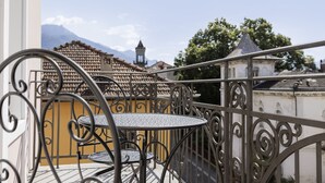 Un balcón con una mesa y sillas de metal, una pared amarilla y vistas a edificios y montañas al fondo.