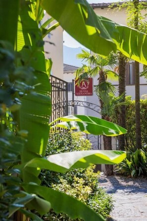 A gated entrance with a sign for Hotel Alexandra, surrounded by lush greenery and a paved path. - Hotel Alexandra (Muralto)
