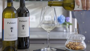Una zona de bar con dos botellas de vino Palmeri, una copa de vino y un tarro de frutos secos sobre una mesa.