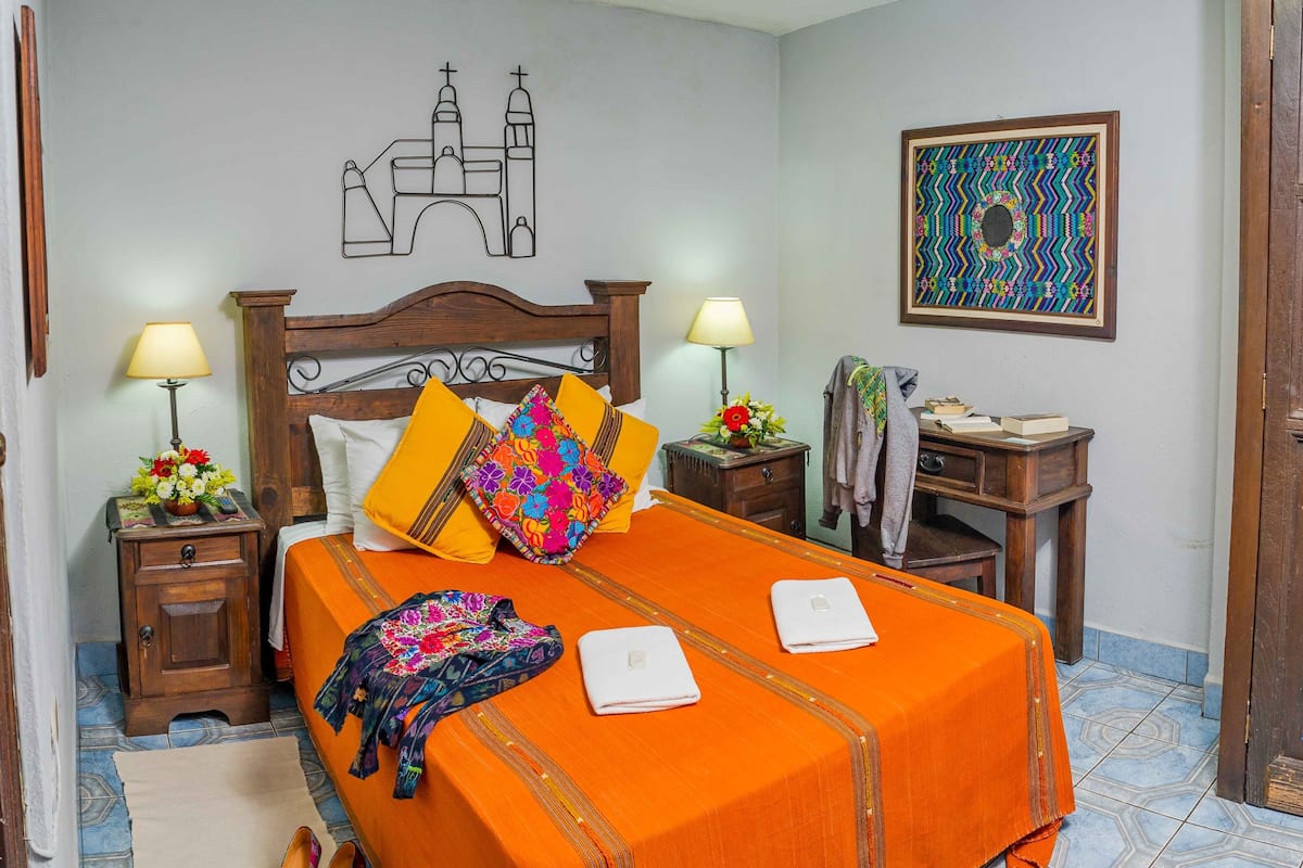 Una habitación de hotel con una cama grande, dos mesitas de noche, un escritorio y una silla.
