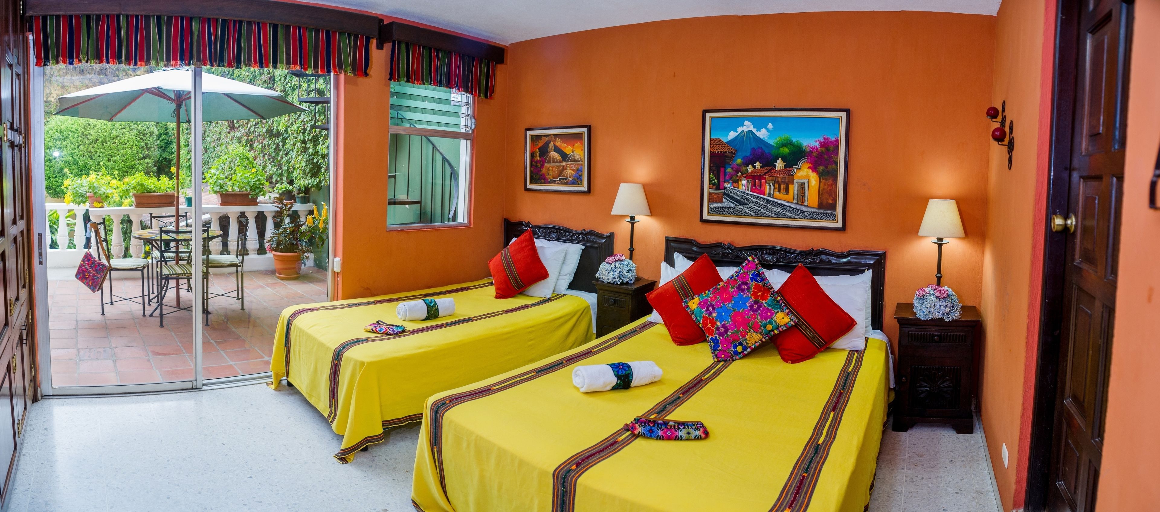 A hotel room with two beds, a balcony with outdoor furniture, and two paintings on the walls.